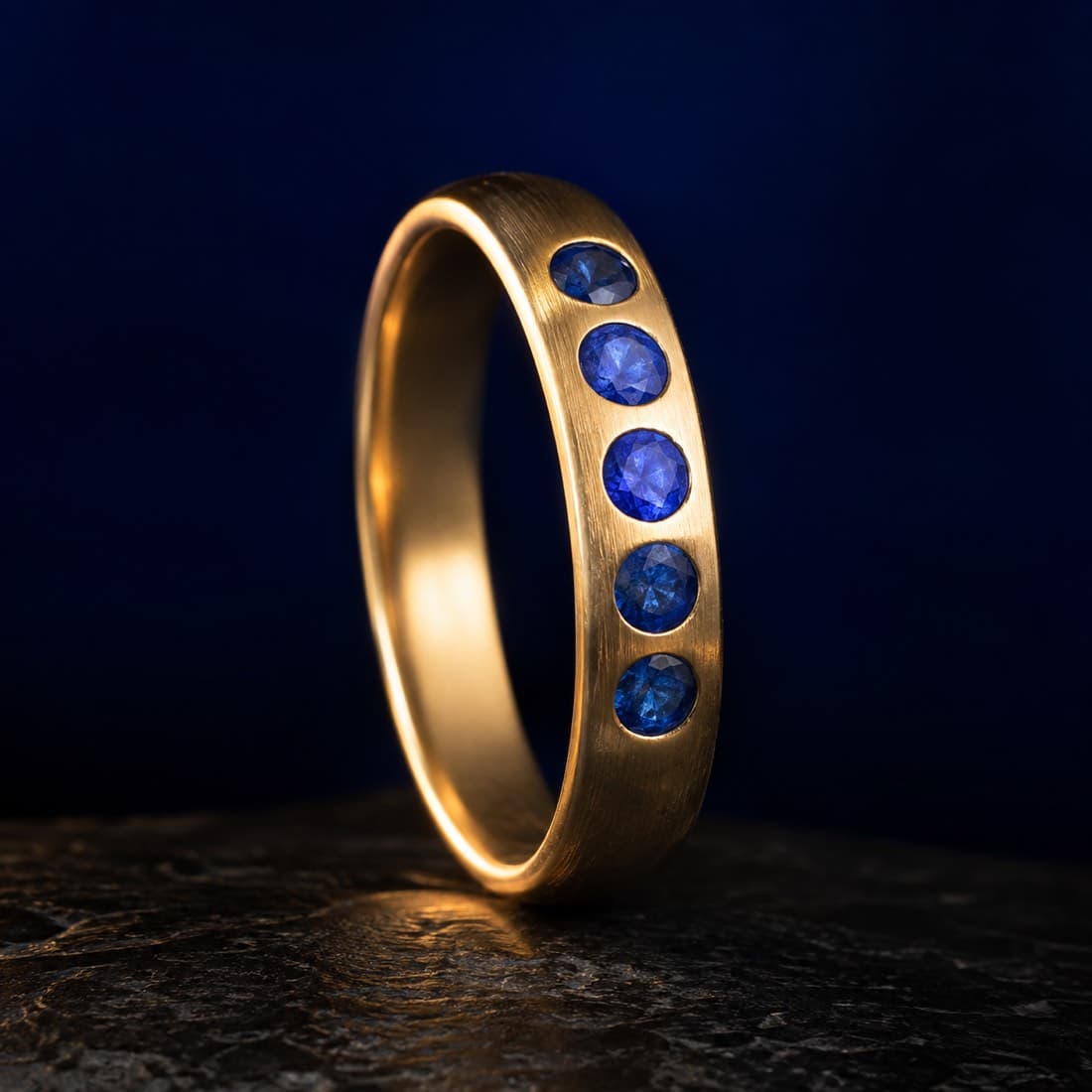 Blue Sapphire Band Ring — 9ct Gold — Five flush-set sapphires along a solid 9ct gold band. 2.8 g, hallmarked.