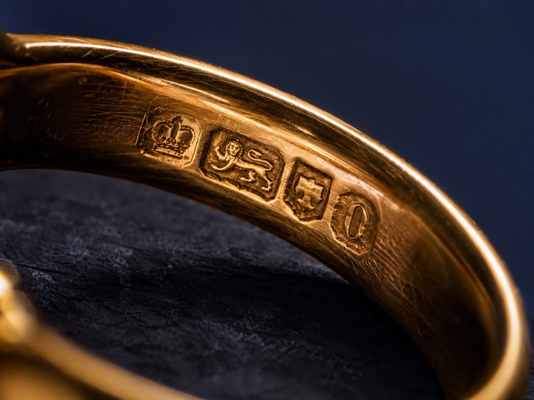 Macro photograph of the inside of a gold band with a row of struck hallmark punches, raking light showing the depth of each strike